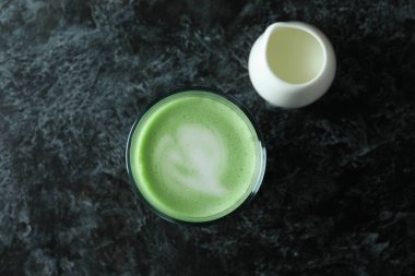 Siyah dumanlı arka planda bir bardak matcha latte ve süt.