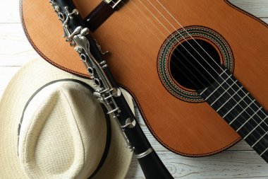 Beyaz ahşap masada klasik gitar, klarnet ve şapka.