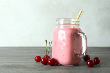 Cam kavanoz vişneli smoothie ve gri desenli masa malzemeleri.