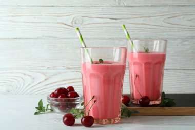 Bir bardak kirazlı içecek ve beyaz ahşap masada malzemeler.