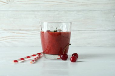 Bir bardak vişneli buzlu içecek, pipetler ve malzemeler beyaz ahşap masada.