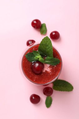 Bir bardak vişneli buzlu içecek ve pembe arka planda malzemeler.
