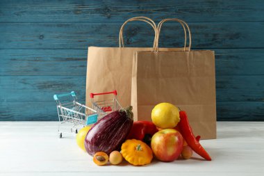 Kağıt torbalar, alışveriş arabaları, sebzeler ve meyveler ahşap masada.