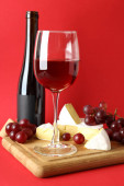 Deska s vínem, sýrem a hroznem na červeném pozadí