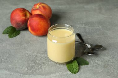 Kavanozlu şeftalili yoğurt, şeftalili ve kaşıklı gri arka plan