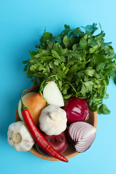 Bowl with spicy vegetables and parsley on blue background