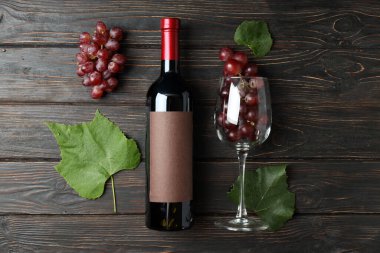 Bir şişe şarap, bir bardak üzüm ve ahşap masada yapraklar.