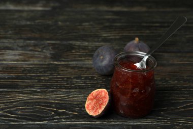 İncir reçeli, kaşıklı kavanoz ve ahşap arka planda malzemeler.