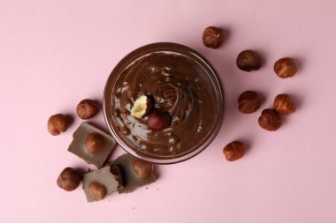 Çukulata ezmeli kase, fındık ve çikolata pembe arka planda.