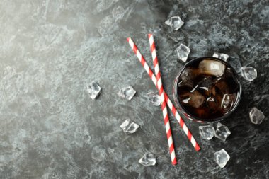 Siyah dumanlı arka planda bir bardak kola, buz ve pipet.