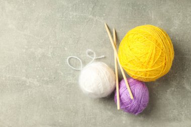 Açık gri arka planda iplik topları ve örgü iğneleri
