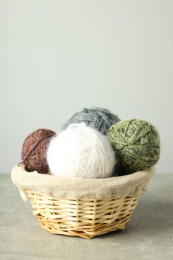 Açık gri masada yün yumakları olan hasır sepet.