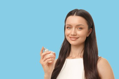 Bir kadın stüdyoda narin bir parfüm şişesini gösterirken gülümsüyor.