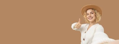 Kadın gülümsüyor ve bir süveter giyerken başparmağını kaldırıyor.