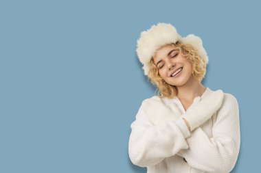 Beyaz bir kazak ve tüylü bir şapkayla gülümseyen kadın.