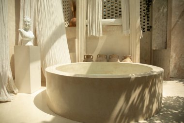 Yuvarlak taş bir küvet ve nazik tekstil içeren zarif bir spa alanı.