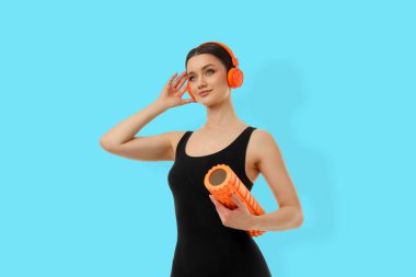 Kadın yoga seansında köpük silindirli ve kulaklıklı.