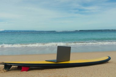 Sahildeki sörf tahtasının üzerinde duran bir dizüstü bilgisayar.