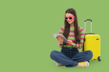 Genç bir kadın bavul ve tabletle yerde oturuyor.