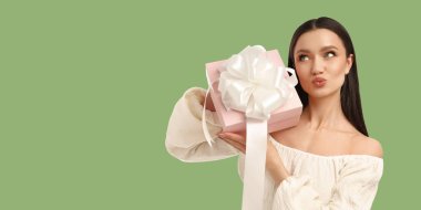 Genç bayanın elinde pembe bir hediye, kocaman bir yay ve gülümseme var.