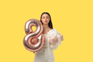 Genç bir kadın kutlama için pembe bir hediye ve balon tutuyor.