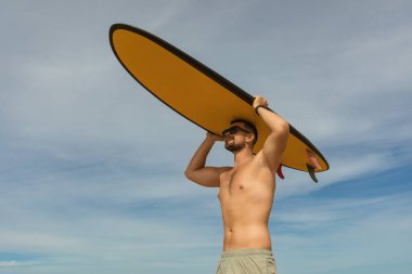 Adam kumsalın tadını çıkarırken sörf tahtasını başının üstünde tutuyor.