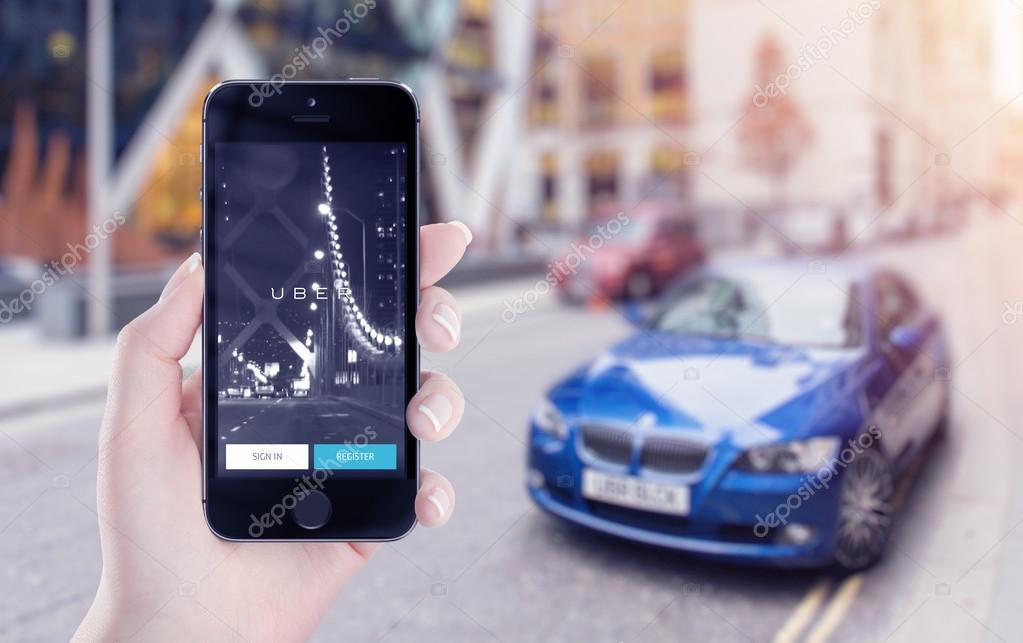 Varna, Bulgaria - May 25, 2015: Uber application startup page on the Apple iPhone 5s display in female hand. Blurred street view with car and flare sun light on the background.