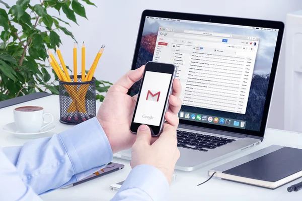 Application Gmail sur l'écran de l'iPhone entre les mains de l'homme et l'écran Macbook Pro — Photo