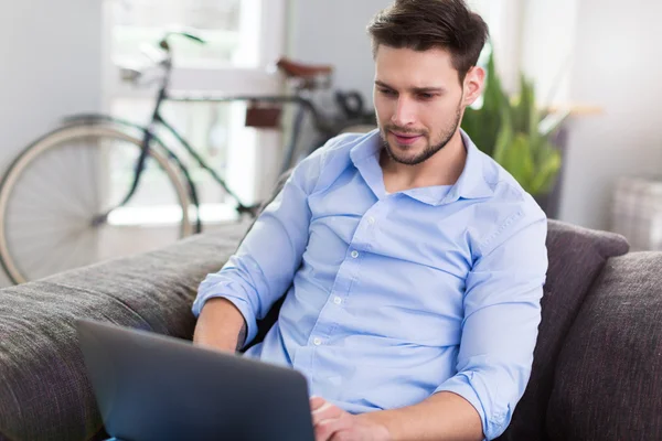 Man sitting on couch with laptop — Stock Photo, Image