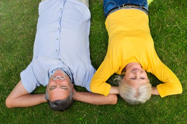 Starší pár, ležící na trávě — Stock fotografie