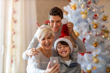Anne ve oğulları evde bir Noel partisinde selfie çekiyorlar.