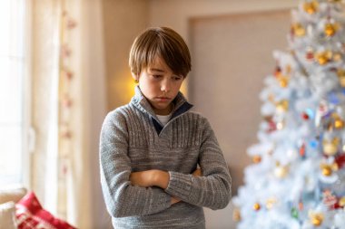 Noel ağacının yanında duran mutsuz çocuk