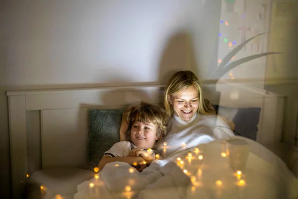 母と息子はベッドで夜一緒にデジタルタブレットを使用して ストックフォト
