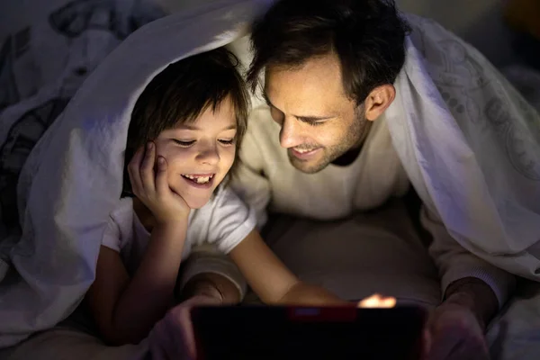 Vater Und Sohn Nutzen Digitales Tablet Nachts Gemeinsam Bett Stockfoto