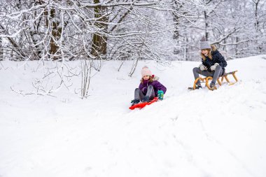 Çocuklar kar yolunda kızakla kayıyor.