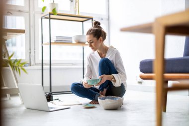 Stüdyosunda dizüstü bilgisayarla çalışan yaratıcı genç bir kadın.