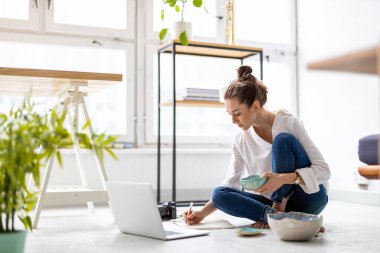 Stüdyosunda dizüstü bilgisayarla çalışan yaratıcı genç bir kadın.