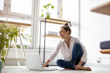 Stüdyosunda dizüstü bilgisayarla çalışan yaratıcı genç bir kadın.