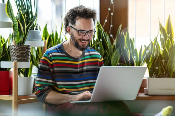 Junger Mann Arbeitet Hause Mit Laptop Inmitten Von Zimmerpflanzen Stockbild