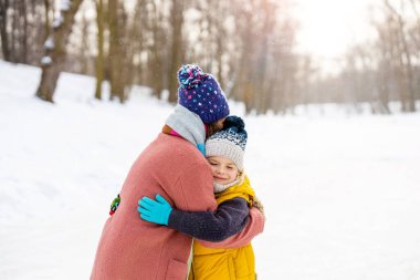 Anne ve oğlu dışarıda karda sarılıyor.