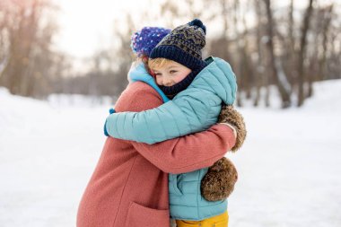 Anne ve oğlu dışarıda karda sarılıyor.