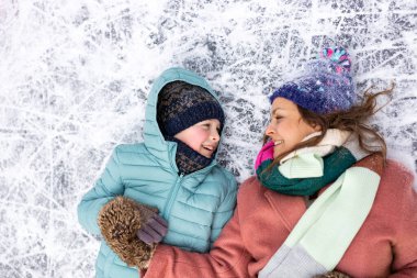 Anne ve oğlu donmuş göl yüzeyine uzanmış gülümsüyor. 