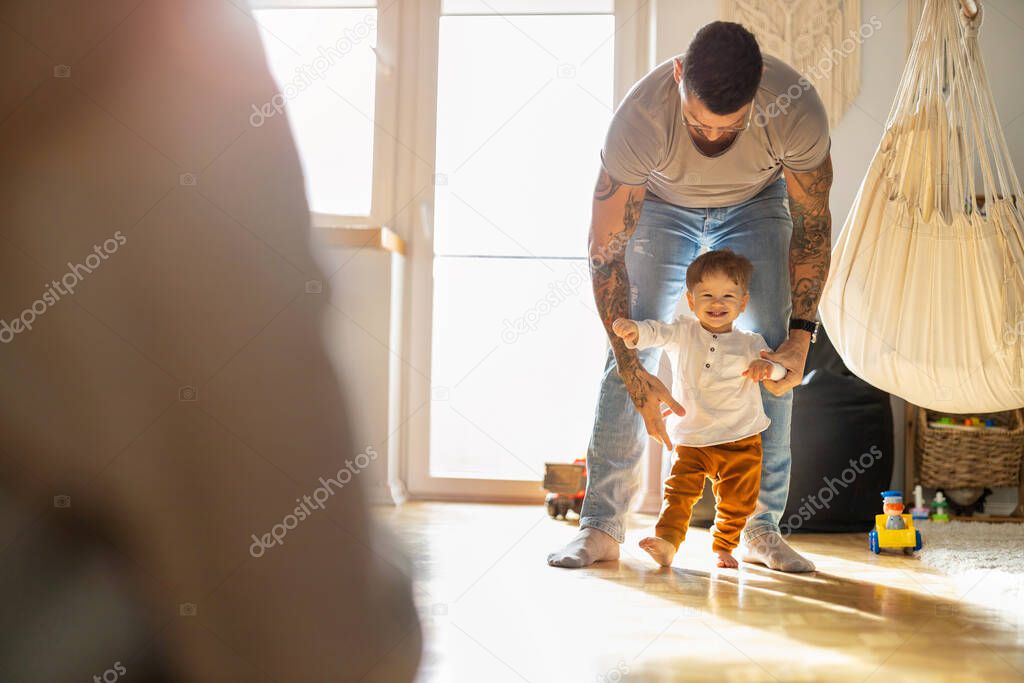Little boy learning to walk with his father next to him at home