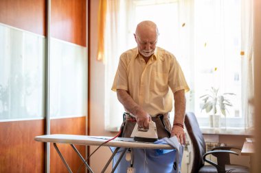 Evde üst düzey bir adam elbiselerini ütülüyor.