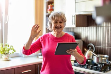 Evde dijital tablet kullanan mutlu yaşlı kadın