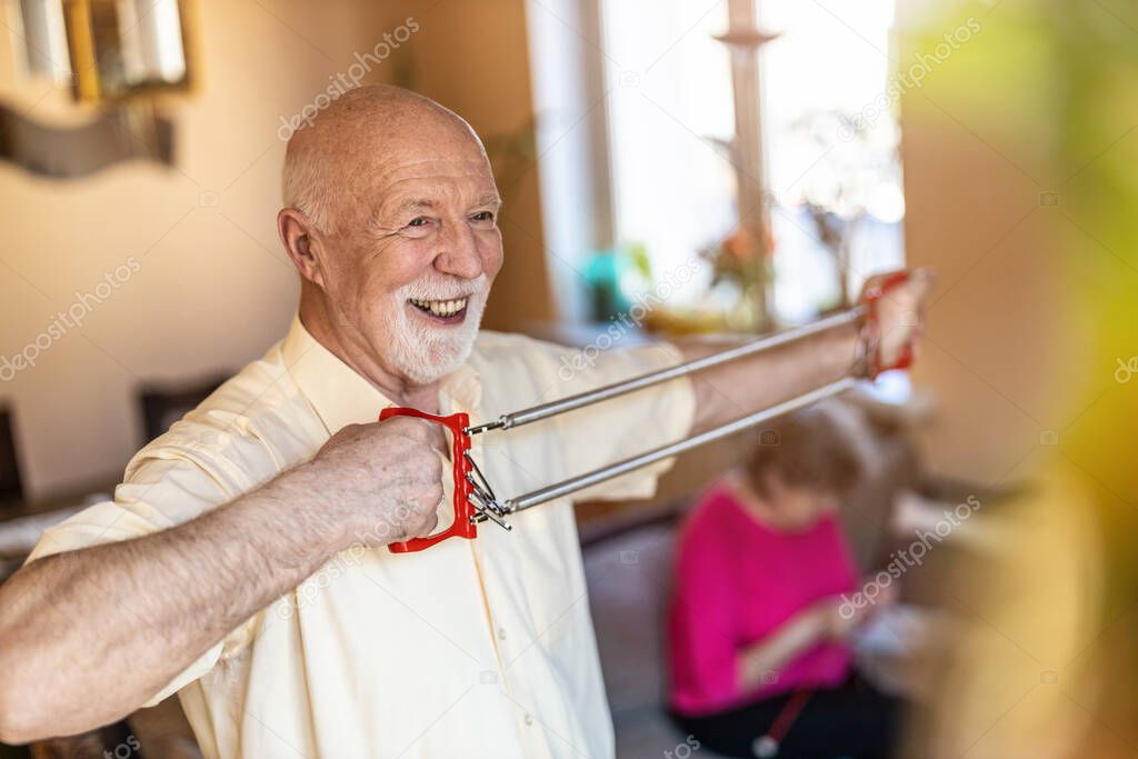 Senior man exercising using chest expander in living room