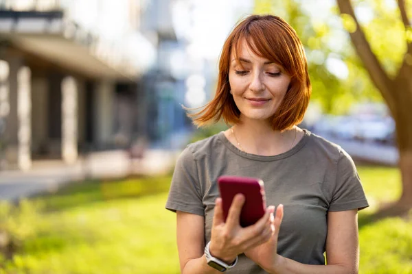 笑顔の女性が市内のスマートフォンを使って — ストック写真