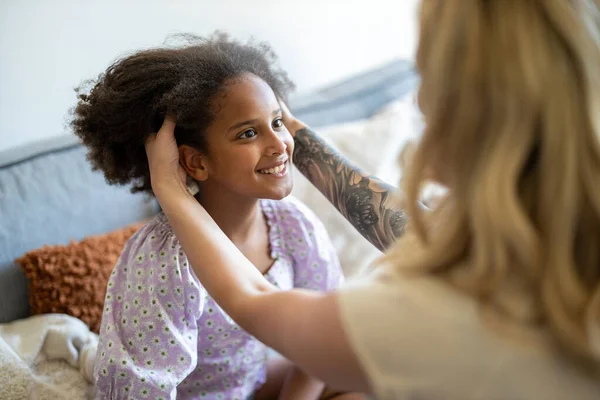 Mother styling daughter\'s hair at home