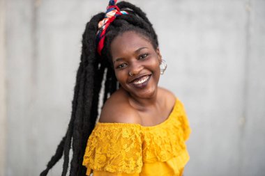 Gri duvarın önünde rastalı saçları olan güzel genç bir kadın.