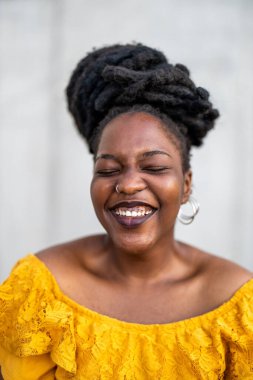 Gri duvarın önünde rastalı saçları olan güzel genç bir kadın.